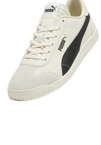 Sneaker bianco con una striscia in suede nero, parte superiore testurizzata, lacci piatti e suola in gomma; presenta un logo Puma prominente sulla linguetta e sul lato.