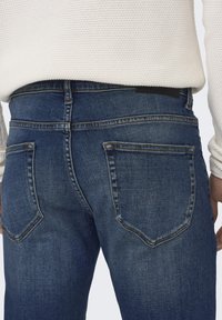 Dunkelblaue Denim-Jeans mit einer taillierten Passform. Verfügt über zwei Gesäßtaschen mit einem dezenten Nähmuster und einem schwarzen Etikett am Taillenbund.