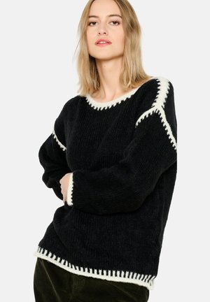 Pull en tricot noir avec une finition texturée, ornée de surpiqûres contrastantes couleur crème le long de l'encolure, des manches et de l'ourlet.