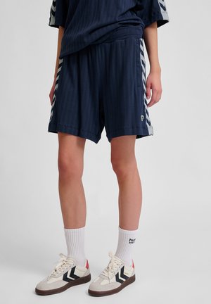Marineblauwe sportshorts met een streeppatroon, met contrasterende zijstrepen. Gecombineerd met witte sokken en lichtgekleurde sneakers met accenten.