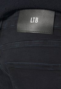 Jeans in denim nero con una patch in pelle etichettata "LTB," caratterizzati da una cucitura a contrasto e una vestibilità aderente.