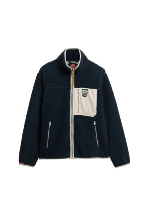 Navy blue fleece jacket with a white front pocket, zippered closures, and a high collar. Features a logo patch on the upper left.
