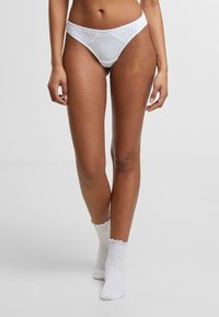 Valge pitsist ääristatud stringtrussikud, millel on sile kangast viimistlus. Rinnal on õrn pitsiline detail.