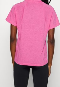 Camiseta de manga corta y corte relajado en tejido rosa jaspeado con un sutil patrón moteado, combinada con mallas negras. Textura suave, ligera.