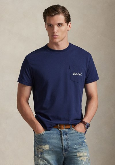 Tumesinine puuvillane t-särk, millel on ümara kaelusega lühikesed varrukad ja rinnatasku, millel on valgega tikkitud "Polo RL". Kandmiseks koos kulutatud teksadega.