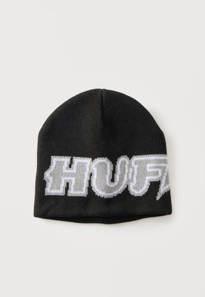 Bonnet en tricot noir avec de grandes lettres stylisées blanches et grises épelant "HUF" sur le devant sur un fond uni.