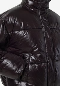 Juoda pūsta striukė su blizgiu paviršiumi, aukštu apykakliu, užtrauktuku uždarymu ir matomomis siūlomomis dalimis; turi šonines kišenes ir lygų tekstūrą.