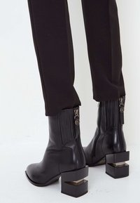 Stivaletti alla caviglia in pelle nera con tacco a blocco strutturato, chiusura con zip sul retro e dettagli a coste intorno alla caviglia.