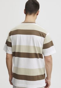 Balta trumpa rankovė t-shirt marškinėliai su horizontaliomis juostelėmis, kurios yra kreminės ir rudos spalvos. Minkšta medvilnė, laisvas siluetas, apvalus iškirpimas, minimalus dekoravimas.
