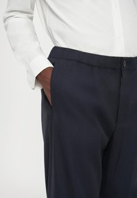 Tumed sinised püksid lõdva lõikega, küljetaskutega ja siledast materjalist. Kombineeritud valge nööbiga särk.