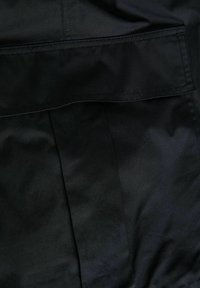 Gros plan sur un tissu noir avec un rabat rectangulaire cousu et une couture verticale.