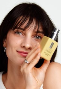 Yellow square bottle with silver pump, labeled "broad spectrum SPF 30," held against a light background, featuring a sleek design.