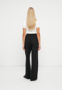 Zwarte wijde broek met een elastische tailleband, gecombineerd met een wit T-shirt met korte mouwen. De outfit heeft een minimalistisch ontwerp en een soepele textuur.