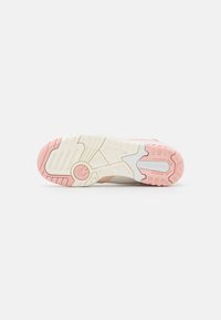 Semelle d'une basket New Balance montrant un motif de bande de roulement rose et blanc avec une adhérence texturée et le nom de la marque sur le talon.