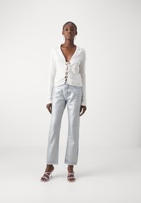 Top blanco de manga larga con cordones en la parte delantera, combinado con jeans rectos metálicos azul claro. Acentuado con tacones de tiras morado claro.