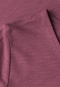 Gros plan sur un tissu mauve chiné montrant des surpiqûres détaillées le long d'un bord plié, mettant en évidence la texture et la qualité de la couture.