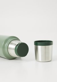 Green insulated water bottle with a metallic silver base and a dark green lid, accompanied by a matching stainless steel cup.