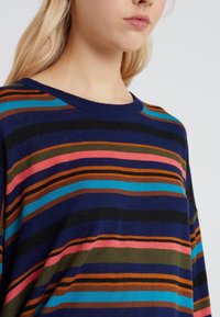 Knitted sweater featuring horizontal stripes in navy, pink, orange, brown, and teal. Round neckline, relaxed fit, and soft texture.