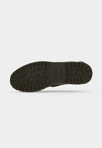 Semelle de chaussure en caoutchouc noir avec de profondes empreintes de pas comprenant des croix et des rectangles, vue de dessous sur fond blanc.