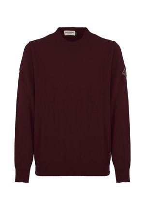 Maglione lavorato a maglia bordeaux con colletto tondo, maniche lunghe e polsini a coste. Presenta una toppa con il logo sulla manica sinistra. Texture morbida.