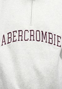 Jasnoszara bluza z suwakiem na ćwierć, z dużym bordowym napisem "ABERCROMBIE" na piersi.