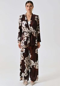 Completo pantaloni floreale marrone fluente in raso, con vita con cintura, maniche lunghe e ampi motivi floreali color crema.