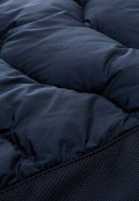 Tissu matelassé bleu marine avec des sections rembourrées en quilt. La texture lisse se transforme en un détail en maille texturé sur le bord inférieur.