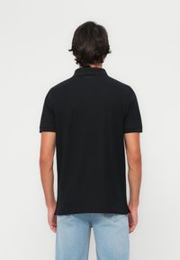 Melnas polo krekls ar īsām piedurknēm. Gluda kokvilnas auduma. Apkaklei un malām ir nedaudz izstrādājumi. Nēsāts ar gaiši ziliem džinsa biksēm.