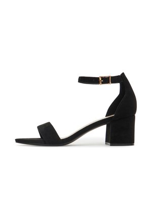 Czarne sandały na słupku z zamszu, z szerokim paskiem na palce i regulowanym paskiem wokół kostki z złotym zapięciem. Płaska podeszwa, minimalistyczny design.