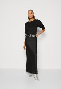 Black puff-sleeve top paired with a sleek black satin skirt. A patterned belt accentuates the waist. The model wears snake-print ankle boots.