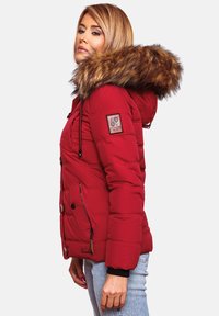 Red puffer jacket with a faux fur hood, quilted texture, front button and zipper closure, and side pockets. Logo patch on upper arm.