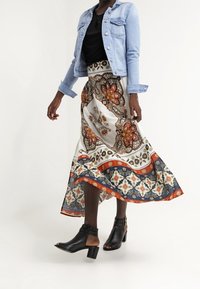 Pitkä, valuva hame, jossa on paisley-printti valkoisena, oranssina ja sinisenä, yhdistettynä vaalean denim-takkiin ja mustiin nilkkapanta-korkokenkiin.