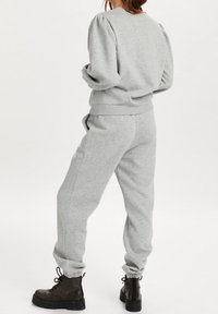 Gray sweatshirt with puffed sleeves and ribbed hem, paired with matching joggers featuring elastic cuffs and side pockets; black lace-up boots.