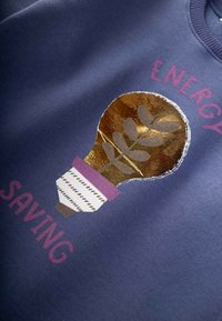 Felpa blu scuro con una grafica d'oro a forma di lampadina con un motivo a foglia e un accento viola, accompagnata dal testo "ENERGY SAVING" in rosa.