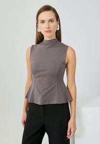 Top peplum cinza com gola alta, design sem mangas, textura suave e silhueta ajustada, usado com calças pretas.