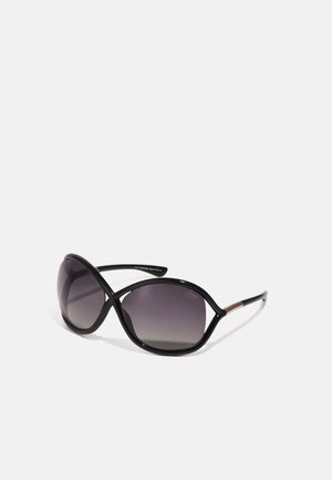 Black sunglasses with gradient lenses, featuring an elongated oval shape and a glossy finish, accented by thin metallic side details.