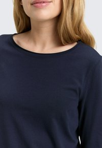 Granatowy długorękawowy shirt z zaokrąglonym dekoltem, wykonany z miękkiego, gładkiego materiału. Charakterystyczne przeszycia widoczne wzdłuż dekoltu.