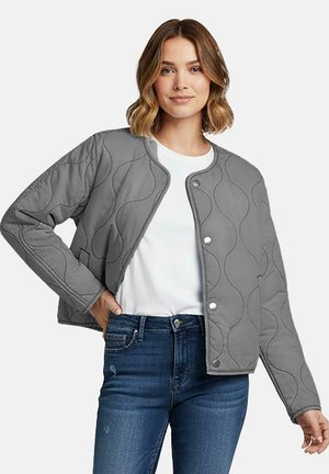 Grijze gewatteerde bomberjack met golvende stiknaden, drukknoopsluiting aan de voorkant en zijzakken, gecombineerd met een wit T-shirt en blauwe jeans.