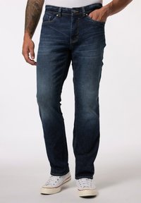 Vaqueros de mezclilla azul oscuro con un diseño de pierna recta, un ligero desgaste, estilo de cinco bolsillos y herrajes metálicos, combinados con zapatillas blancas.