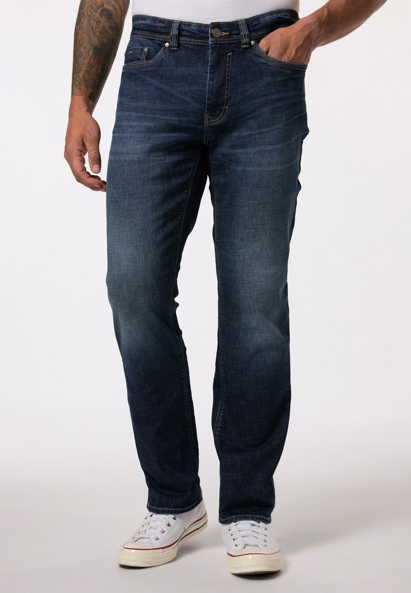 Vaqueros de mezclilla azul oscuro con un diseño de pierna recta, un ligero desgaste, estilo de cinco bolsillos y herrajes metálicos, combinados con zapatillas blancas.