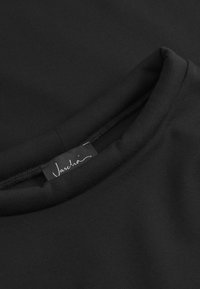 Obleka iz črnega blaga z okroglo ovratnikom in gladko teksturo, z majhno oznako blagovne znamke, ki prikazuje "Vaschio" v belem pisanim besedilu.