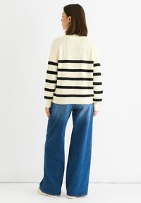 Cream knit sweater with black horizontal stripes, featuring a ribbed design and a relaxed fit, paired with wide-leg blue jeans.