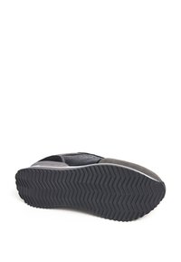 Zool van een grijze en zwarte sneaker met een zigzagprofiel, die textuur en grip toont, evenals een deel van het bovenwerk van de schoen.