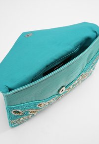 Clutch de tela turquesa con adornos de cuentas y perlas, cierre magnético, y bolsillo interior etiquetado como Vero Moda.