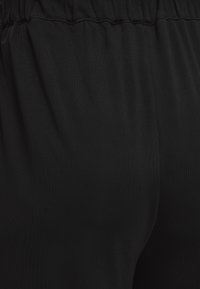 Gros plan d’un tissu noir avec une ceinture élastique, montrant la texture et de légers plis dans le matériau.