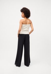 Top creme sem alças com um padrão texturizado, combinado com calças largas de cintura alta pretas e sapatos pretos, visto por trás.