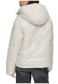 Puchowa kurtka w odcieniu off-white, z dużym kapturem, skośnym wzorem pikowania i luźnym krojem. Miękki, błyszczący materiał z prążkowanymi akcentami.