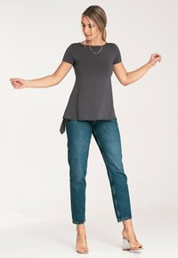 Szary top z krótkim rękawem i rozkloszowanym dołem oraz bocznym wiązaniem, zestawiony z niebieskimi dżinsami prostymi i przezroczystymi sandałami na blokowym obcasie.