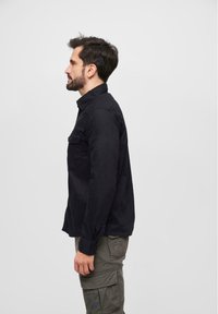 Black long-sleeve shirt with a button-down collar and chest pocket, featuring a smooth texture and a relaxed fit, worn with gray cargo pants.