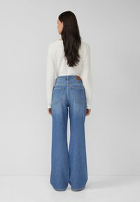 Hellblaue weite Jeans mit hoher Taille, ausgestattet mit einem beigefarbenen Lederpatch auf der Rückseite und zwei Gesäßtaschen.